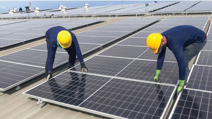 Two workers wearing yellow safety helmets installing solar panels on a rooftop as part of a solar energy project.