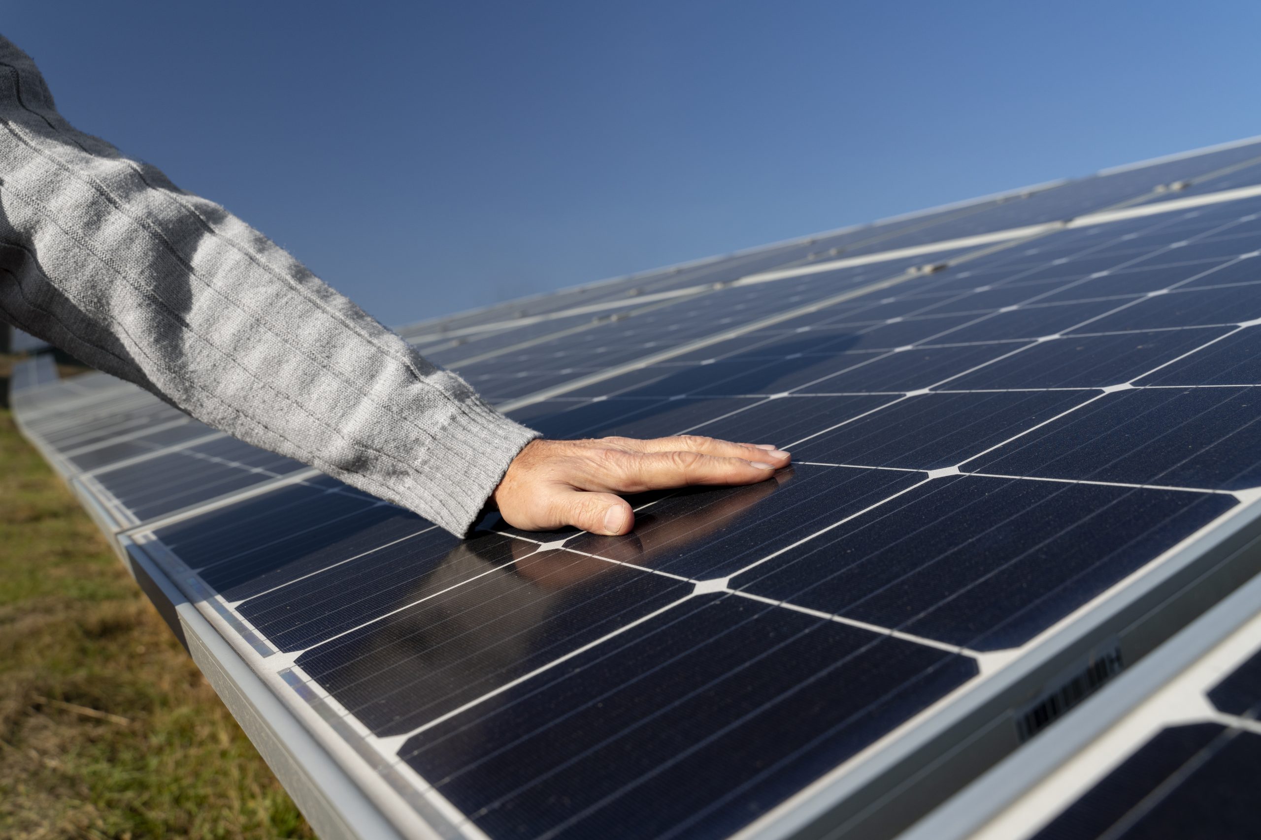 Person inspecting a solar module by placing a hand on the surface of the panel under clear sunlight.