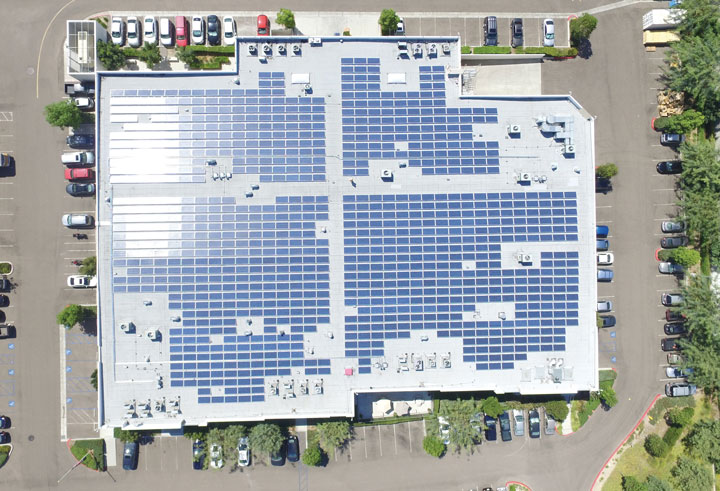 Aerial view of a commercial building rooftop covered with solar panels surrounded by a parking lot.