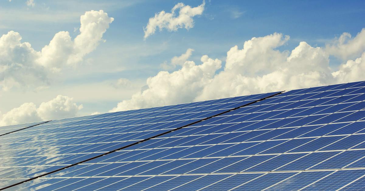 A wide view of solar panels installed outdoors under a bright sky with clouds.