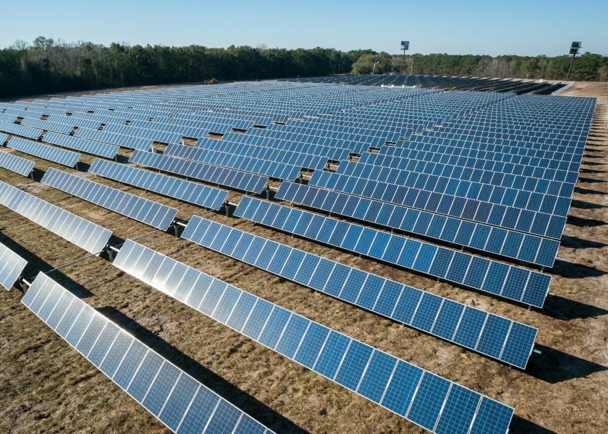 A large solar power plant featuring multiple rows of ground-mounted solar panels installed across open land.