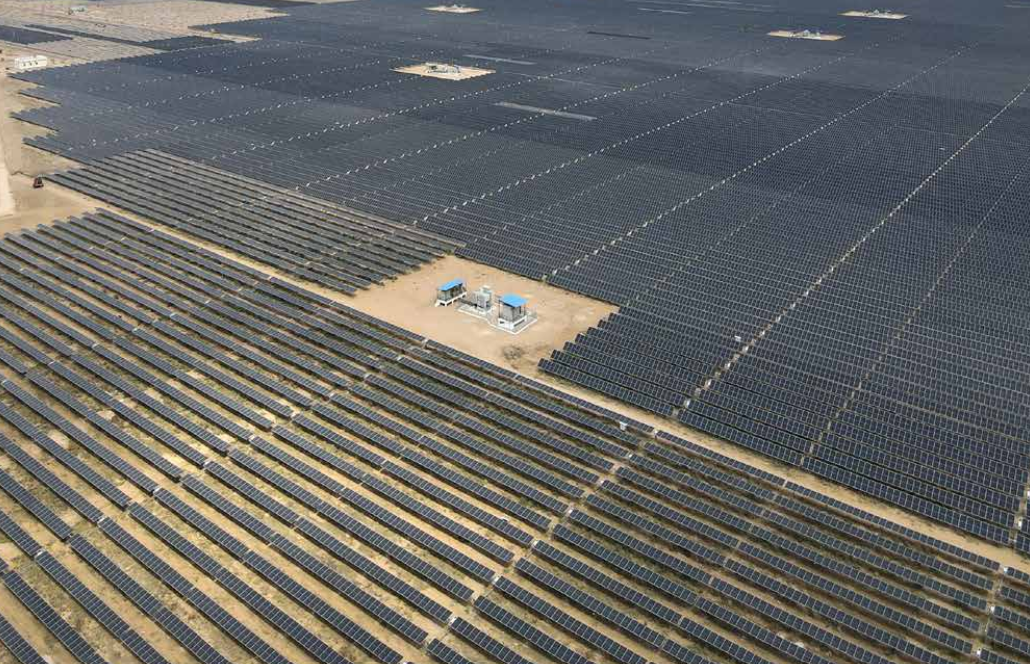A wide aerial view of a large utility-scale solar farm with rows of solar panels installed across open land.