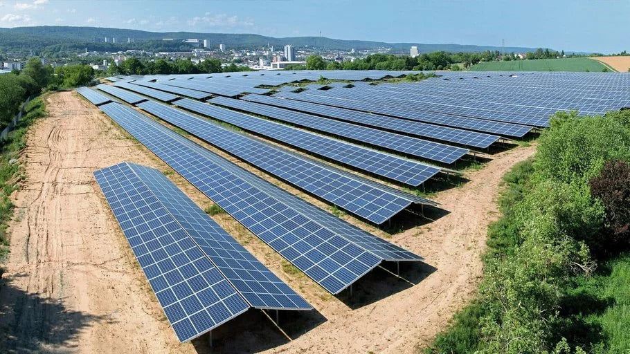 Rows of solar panels installed on open land near a city landscape under a clear sky.